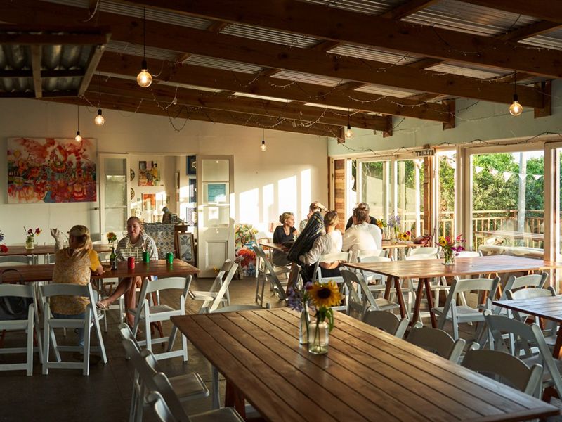 The indoor dining room: long wooden tables, white folding chairs, sunflowers in jars, fairy lights across the beams and paintings on the walls.