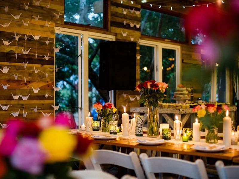An evening reception table set with roses, candles and paper cranes hanging against a timber wall.
