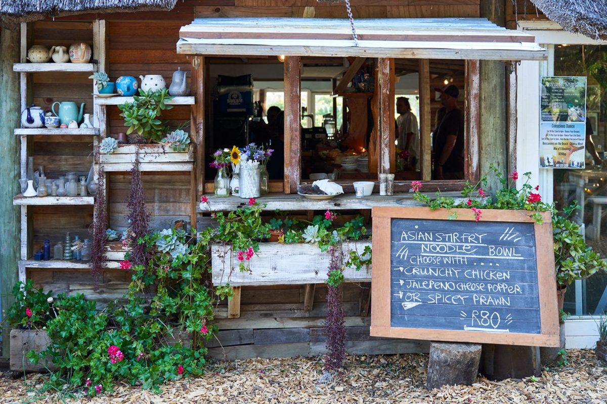 The café's rustic wooden serving hatch, shelves of teapots and china, potted succulents and a chalkboard specials board.